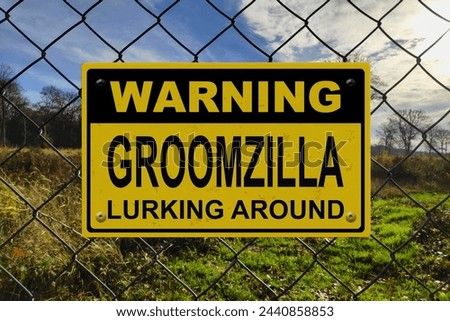 Black and yellow warning sign on a fence with the message "Warning - Groomzilla lurking around".