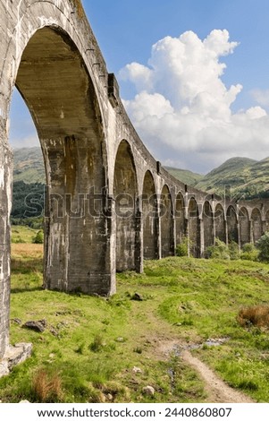 Vertical shot of Glenfinnan Viaduct with its imposing arches cutting a striking figure against the Highland's rolling hills and a dynamic sky. Scotland
