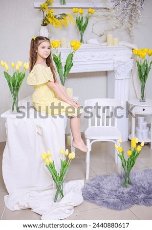 Cute girl in a yellow dress with a bouquet of purple flowers on a background of yellow tulips. Congratulations on Mother's Day, Women's Day, March 8