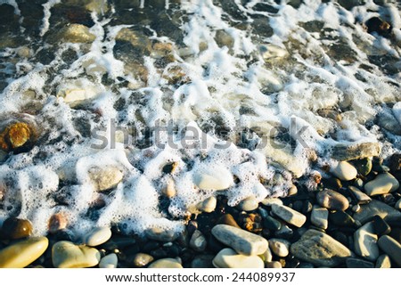 Wave of the ocean sea on the pebble stone beach at the sunset light. Close up view.