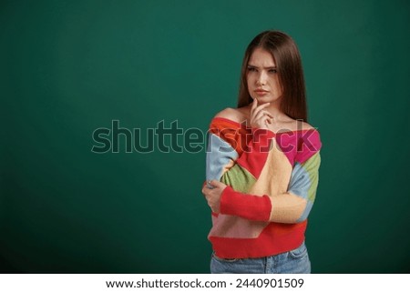 Thoughtful facial expression. Young woman is standing against green background in the studio.
