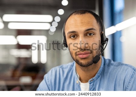 Portrait of a young Arab man sitting in a headset in front of a laptop in the office and confidently looking at the camera. Close-up photo.