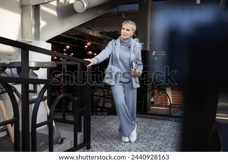 Attractive and stylish mature woman in grey pant suit with jacket and turtleneck, accessorized with handbag and white shoes. The perfect look for successful women over 50. Royalty-Free Stock Photo #2440928163