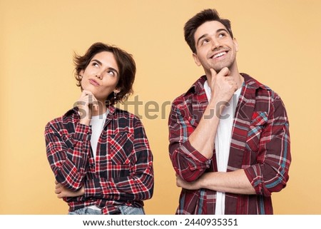 Portrait photo of a thoughtful couple, with a dreaming woman and a smiling man, thinking deeply about an idea, crossing their arms, posing isolated on a yellow background, and looking away