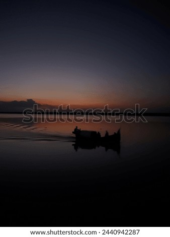 A little boat is shown drifting on a placid body of water in this picture, which shows a beautiful sunset view. The boat has a single sail, a straightforward design, and is meant for one person only. 