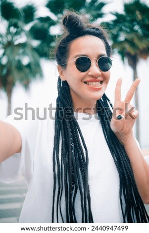 Young caucasian pretty woman shows V sign making selfie with happy smile with ocean beach palms on background.Vertical photo High quality photo