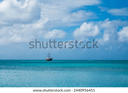Pirate ship (tour boat) on the open turquoise water of the Caribbean Sea. Landscape photo of horizon and sky beautiful white clouds taken from Palm Beach, Noord, Aruba, Dutch island (February 2024). Royalty-Free Stock Photo #2440956451