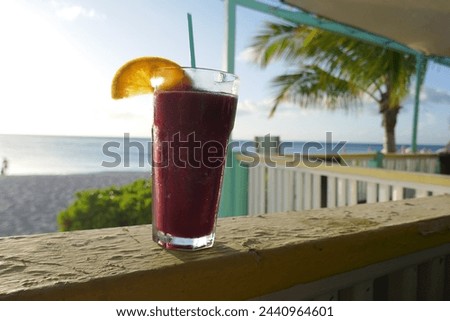 Tropical frozen drink with orange slice and ocean beach scene in background 