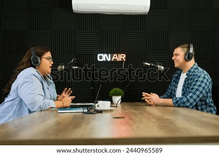 Cheerful podcast co-hosts smiling looking happy while recording an episode of their talk show at the radio studio