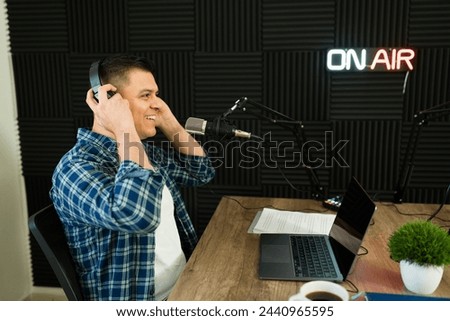 Smiling handsome latin man putting on the headphones to start recording a podcast episode or radio show in the studio Royalty-Free Stock Photo #2440965595