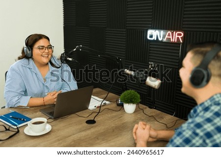 Excited woman broadcast with a radio talk show recording while talking with a guest for a podcast episode Royalty-Free Stock Photo #2440965617
