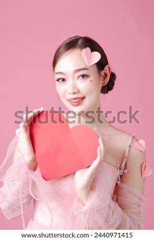 Attractive young Asian woman feels happy and romantic showing heart model expresses tender feelings poses against pink background. People affection and care concept. Royalty-Free Stock Photo #2440971415