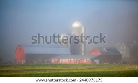A red barn with silver silos in heavy fog on a farm in rural Vermont. Royalty-Free Stock Photo #2440973175