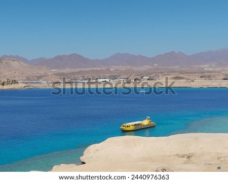 seascape with mountains on the horizon and turquoise water, sandy beach and  yellow submarine.
