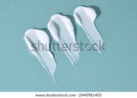 Three strokes of white cream on a blue background. Royalty-Free Stock Photo #2440981405