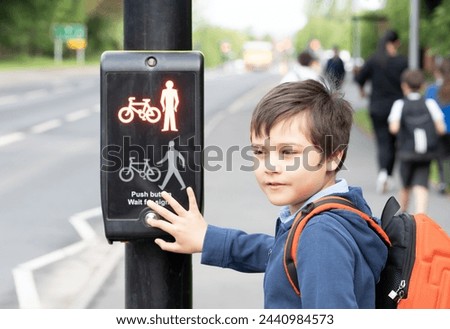 School kid pressing a button at traffic lights on pedestrian crossing on way to school. Child boy with backpack using traffic signal controlled pedestrian facilities for crossing road.