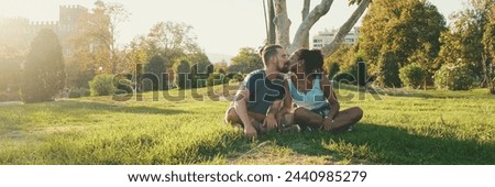 Happy smiling interracial couple talking while sitting on the grass in the park, Backlight, Panorama