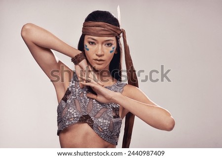 Portrait, girl and Native American culture in studio with warrior makeup, confidence and tribe style. Indigenous fashion, face paint or woman in First Nations clothes on white background with feather