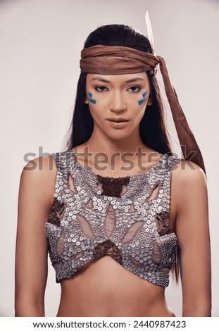 Portrait, woman and Native American culture in studio with warrior makeup, confidence and tribe style. Indigenous fashion, face paint or girl in First Nations clothes on white background with feather