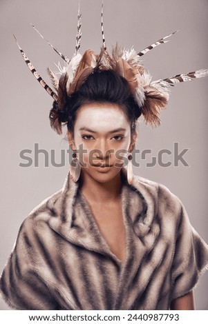 Woman, portrait and art with fashion of Native American in traditional clothing on a gray studio background. Female person with feather, face paint or stylish tribal outfit of goddess in beauty