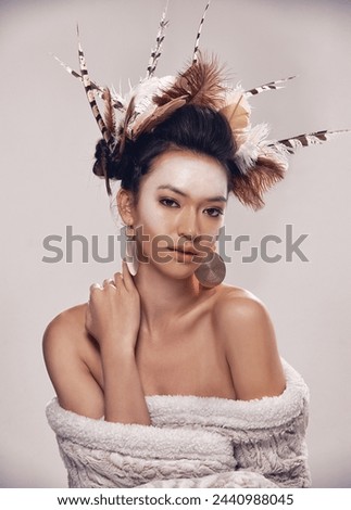 Woman, portrait and native american headdress in studio with feather, hair and beauty with culture cosmetics. Model, face and indigenous make up or art and elegant fashion or cloth on grey background
