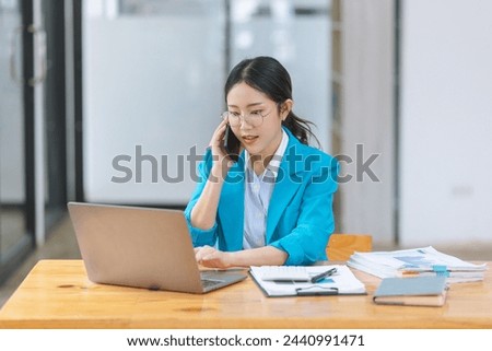 Asian businesswoman wearing a blue suit using smartphone with digital laptop computer working at modern office, Asian beautiful businesswoman in blue suit working in the modern office.