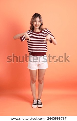 The young Asian woman in casual clothes with gesture of pointing on the orange background 