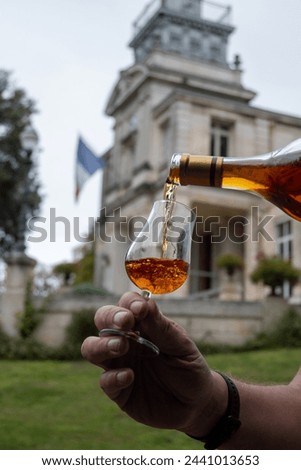 Tasting of aged in barrels cognac alcohol drink and view on old streets and houses in town Cognac, Grand Champagne, Charente, strong spirits distillation industry, France Royalty-Free Stock Photo #2441013653