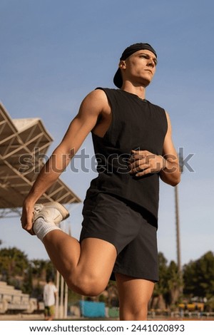 Young male athlete warming up his legs and stretching. Preparing for competition in a sports facility. Vertical photo