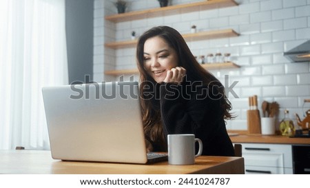Cozy asian woman sitting in the kitchen using laptop computer surfing web, shopping on internet, use social media apps. Modern device usage concept