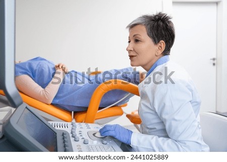 A relaxed female patient lies on an examination bed during an ultrasound, while the attentive doctor operates the sonography equipment with the monitor displaying the image. High quality photo