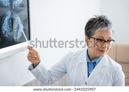 Smiling radiologist pointing at mammogram results on a lightbox. High quality photo