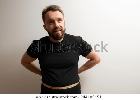 Belly fat problem concept: middle aged bearded hipster measures his waist size and doesn't like the results Royalty-Free Stock Photo #2441031511