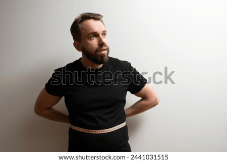 Belly fat problem concept: middle aged bearded hipster measures his waist size and doesn't like the results Royalty-Free Stock Photo #2441031515