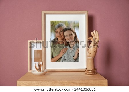 Family portrait of mother and daughter in photo frame on table near color wall