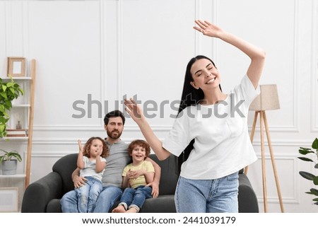 Happy family having fun at home. Mother dancing while her relatives resting on sofa