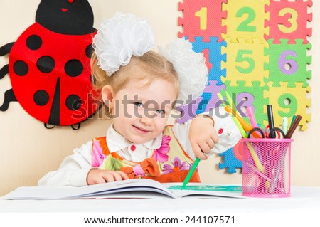 Cute child girl drawing with colorful pencils and felt-tip pen in preschool at table in kindergarten