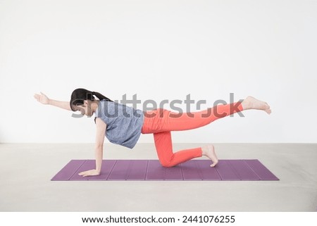 

Full-length view of a young Japanese woman in a living room in a stretch, exercise, workout, yoga, or core training pose.