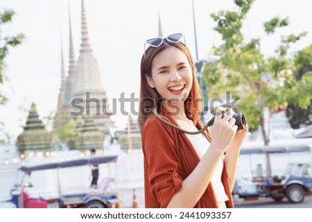 Young Asian woman traveler wearing orange shirt with taking picture using a camera at temple. summer tourism concept.