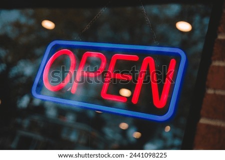 A neon sign reading open in a window with brick on the side.