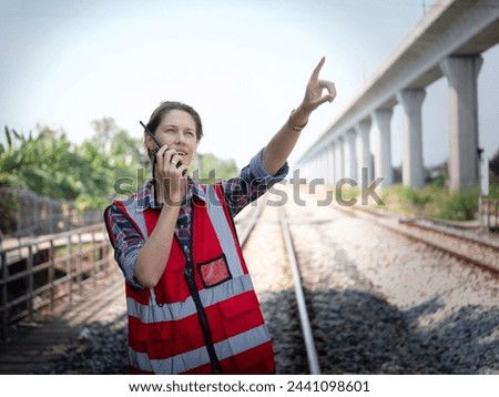 Woman railway engineer use walkie-talkie talking in to talk to maintenance department at site work of train garage. Royalty-Free Stock Photo #2441098601
