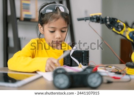 A young girl is sitting at a desk with a robot toy in front of her. She is writing in a notebook, possibly about the robot or her thoughts on it. Concept of curiosity and creativity