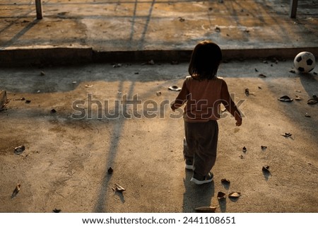 Asian boy plays football on the cement ground. boy plays in the outdoor taken from the back side.