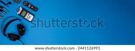 Banner, layout of accessories for recording and listening to sound: headphones, voice recorders, microphone, cables on blue background, top view. Concept of recording pure sound. Copy space Royalty-Free Stock Photo #2441126991