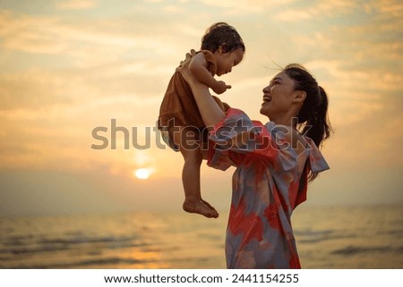 happy mother holding and lifting with her toddler baby girl on the sea beach at sunset Royalty-Free Stock Photo #2441154255