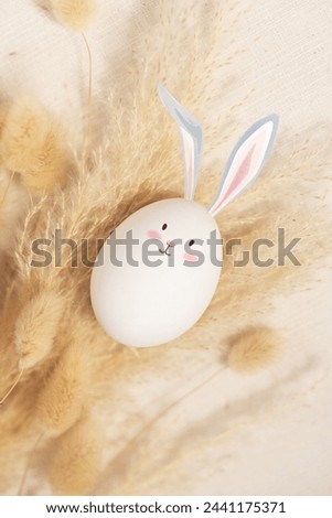 White egg with rabbit ears and face A bunny shaped Easter egg sits on the fluffy grass.