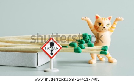 Funny ginger toy kitten with raised paws next to open matchbox and Danger warning sign. Concept of teaching children fire safety rules. Light background. Selective focus. Close-up