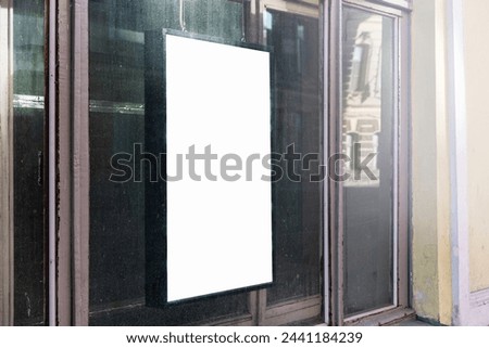 Vertical blank advertisement board on dusty storefront window in urban setting. Reflective glass surface shows city life, ideal for marketing mockup and urban design presentation.