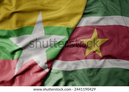 big waving national colorful flag of suriname and national flag of myanmar . macro