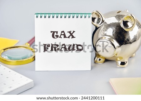 TAX FRAUD on a white notebook on a gray background near a piggy bank, a calculator and stickers